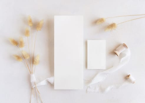 Blank cards near silk ribbons and dried hare's tail grass top view on white, mockup. Boho romantic scene with vertical cards. Bohemian or close to nature greeting or wedding Invitation