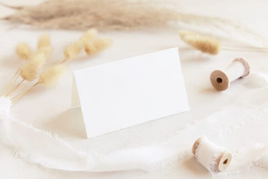 Folded card near silk ribbons and dried hare's tail and pampas grass close up on white, mockup. Boho romantic scene. Bohemian or close to nature greeting or wedding table place