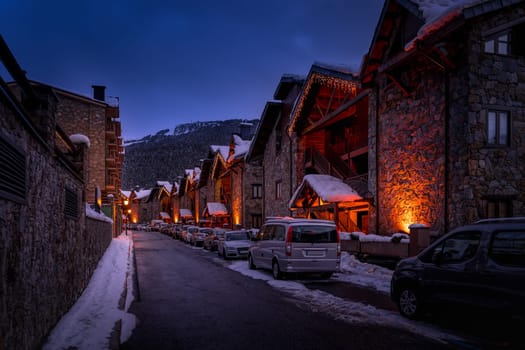 Modern stone houses and apartments illuminated by street lights in El Tarter village at dusk or night fall in Pyrenees mountains, Grandvalira, Andorra