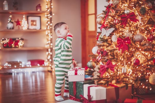 Little boy in pajama standing near the Christmas tree. Concept of the Christmastime and New Year eve.