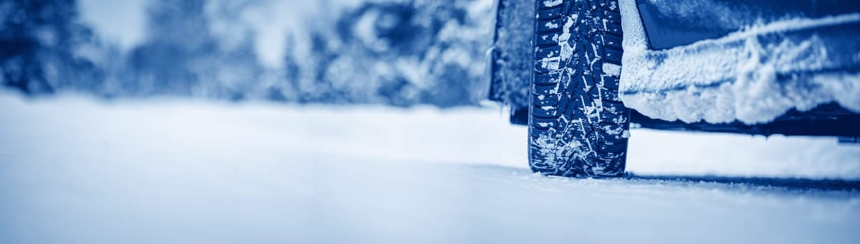 Closeup view of the car's wheel on the snowy road in natural park. Beautiful panoramic view.