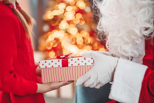 Hands of Santa Claus giving giftbox to the child. Concept of Christmas and New Year.