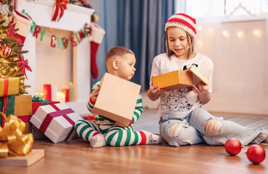 Sister and brother sitting on the floor near Christmas tree indoors. Concept of love, family relation and the celebration Christmas and New Year.