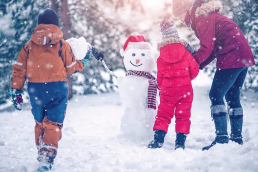 Family bilding a cute snowman in the snowy park. Concept of the family vacation and weekend together.