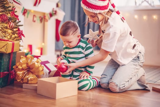 Sister and brother sitting on the floor near Christmas tree indoors. Concept of love, family relation and the celebration Christmas and New Year together.