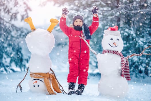 Happy smiling child standing with snowmen in the natural park. Concept of the family vacation and weekend together.