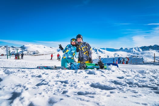 Couple, skier and snowboarder sitting on the snow and looking at camera, Pyrenees Mountains. Winter ski holidays in El Tarter, Grandvalira Andorra