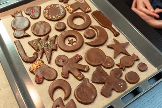 Christmas and New Year cookies of different shapes in the process of decoration with a multi-colored sprinkling on a baking sheet.
