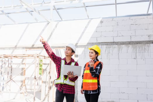 Asian engineer foreman worker man and woman working at building construction site use laptop and talking with radio, engineering hold computer and radio discuss and control worker employee to building