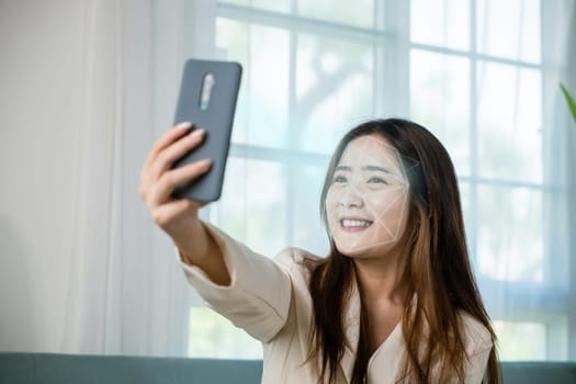 Asian women use smartphone for access control face recognition in private identification on sofa living room at home, Asian female checking her personal data scanning face by mobile phone to unlock