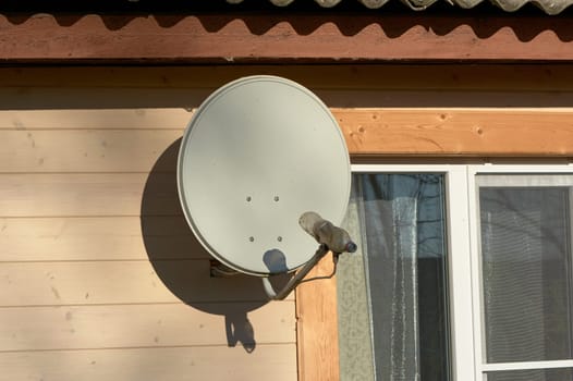 A satellite dish is hanging on the wall of a wooden house. High quality photo