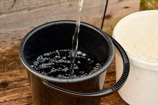 a black plastic bucket is filled with water from the pump. High quality photo