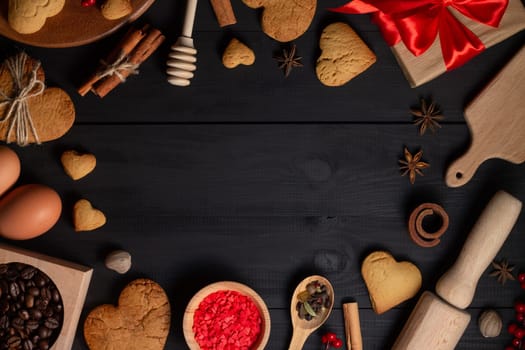 Gingerbread heart shaped cookies, spices, coffee beans and baking supplies on black wood background, copy space