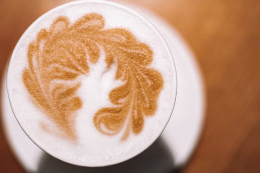 Delicious cappuccino coffee in cup mug glass latte with sour cream milk foam with pattern spike spica on white ceramic plate. Blurred brown table background. Lactose-free. Close up. Top view