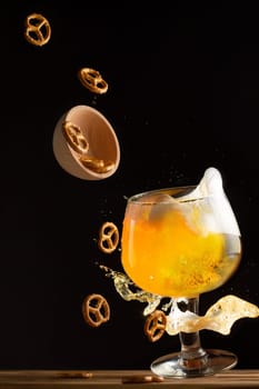 Glass with splashing beer and flying salty pretzels, on dark background. Vertical
