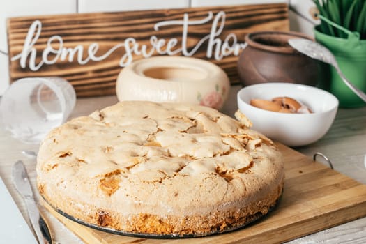 Baked apple pie stands on kitchen counter next to ingredients, cooking utencils, and wooden sign Home sweet home