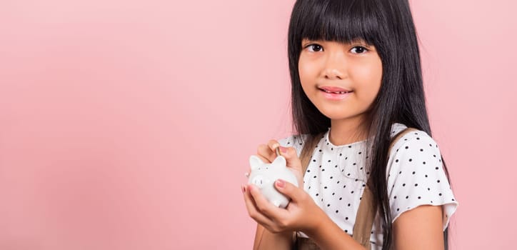 Asian little kid 10 years old holding piggy bank and looking at camera at studio shot isolated on pink background, Happy child girl lifestyle smiling with is full piggybank, Personal money savings
