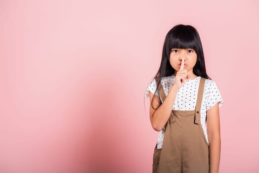 Child secret. Asian kid 10 years old holding finger on lips symbol of hush gesture of asking quiet at studio shot isolated on pink background, Happy children girl show shh with finger at mouth gossip