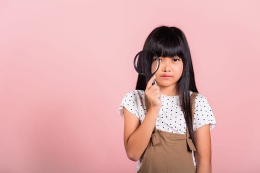 Asian little kid 10 years old funny looking through magnifying glass at studio shot isolated on pink background, Happy child girl lifestyle smiling exploring holding magnifier searching