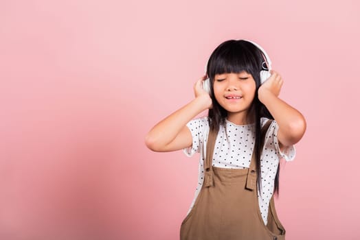 Asian little kid 10 years old smiling listening music wearing wireless headset at studio shot isolated on pink background, Happy child girl lifestyle listen music with headphones keeping eyes closed