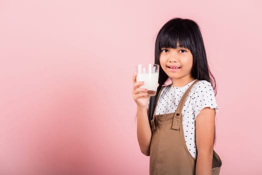Asian little kid 10 years old smile hold milk glass drink white milk at studio shot isolated on pink background, Happy child girl daily life health care Medicine food
