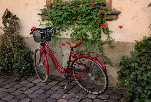 A bright red ladies bike with basket on a house wall.
