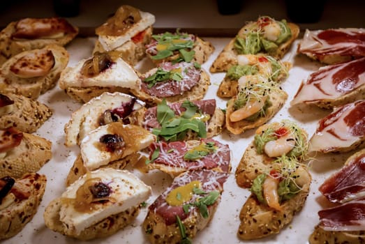 Many tapas, small baguettes pieces with toppings on a board.