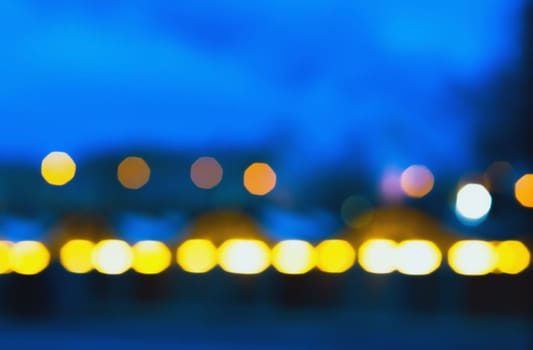 Abstract blurred background of defocused city lights at night. Colorful glowing bokeh of street lighting against a dark blue night sky. Space for copy text or design.