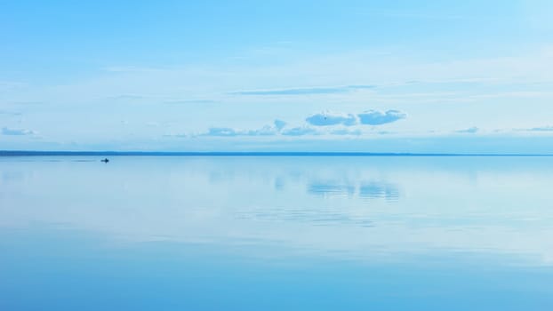 Light blue sky reflected in a calm smooth lake surface. Atmosphere of serenity and tranquility. Summer seascape background with space for copy. Russia, Vologda Oblast, Lake Beloye.