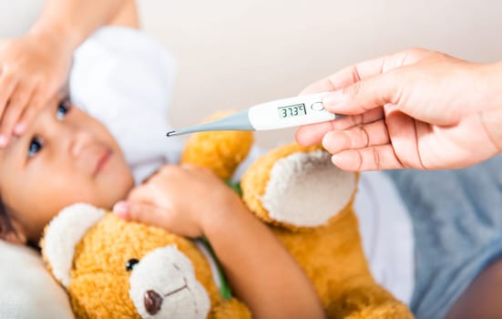 Sick kid. Mother parent checking temperature of her sick daughter with digital thermometer in mouth, child laying in bed taking measuring her temperature for fever and illness, healthcare
