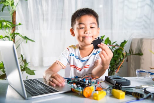 Little student child holding stepping motor to assemble car toy, Asian kid boy assembling the Arduino robot car homework project at home, education AI technology workshop school learning lesson