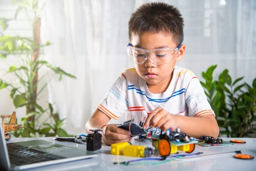 Asian kid boy plugging energy and signal cable to sensor chip with Arduino robot car, Little child remotely learn online with car toy, STEAM education AI technology course school learning lesson