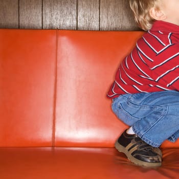Caucasian boy kneeling on vinyl sofa.