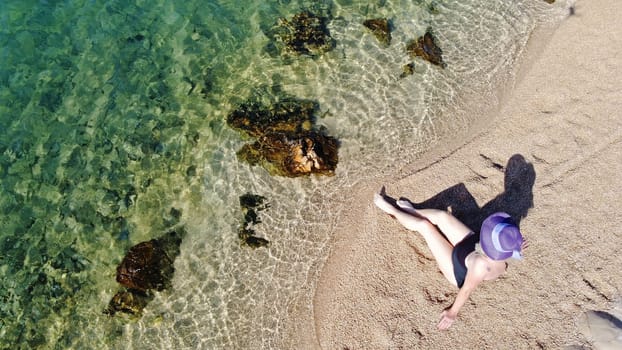 Woman in swimsuit and straw hat sits in the sand by the sea