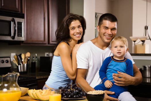 Caucasian family with toddler son in kitchen at breakfast smiling at viewer.