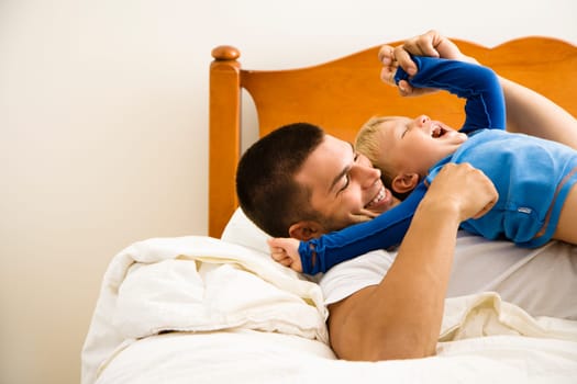 Caucasian toddler boy and father playing and tickling in bed.