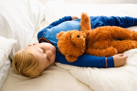 Caucasian toddler boy sleeping in bed with teddy bear.