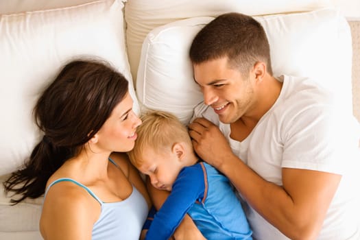 Caucasian mid adult parents with toddler son sleeping in bed.