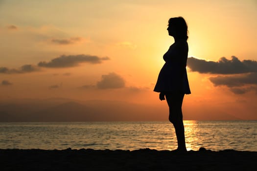 Pregnant woman standing on the beach at sunset
