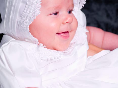 A portrait of a baby girl in a christening dress on a dark background. This photo has a shallow depth of field and the focus is on her eye.