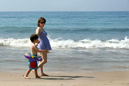 Pregnant mother and her son walking on the beach