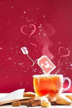 Tea bag with hearts and inscription Love on label above tea mug with splashes and heart shaped steam on dark red background. Copy space