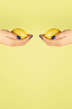 Two open female hands with blue nails holding fresh lemons opposite each other isolated on yellow. Creative art concept. Food minimal colorful concept. Vertical. Copy space. Mock up.