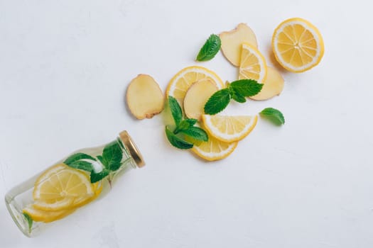 Glass bottle with lemonade and ingredients for cooking. Ginger, lemon, mint on white surface. Flat lay, top view