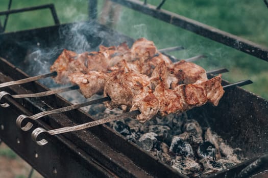 Raw grilled meat on skewers is cooked on charcoal grill. Cooking barbecue outdoors