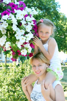 daughter sitting on her mother and many flowers in the city park