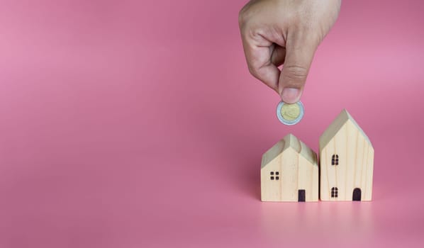A human hand put a coin in the model house. Ideas for saving money to buy a new home and loans for planning future real estate investments.