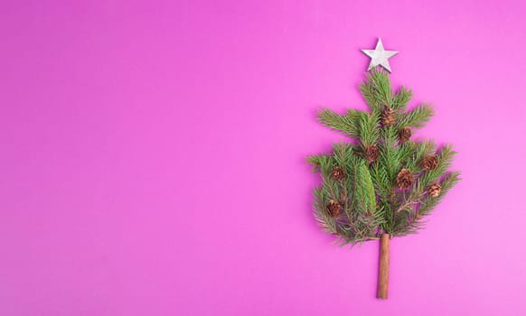 Christmas tree made from fir branches, pine cones and a cinnamon stick as the trunk, pink greeting card with copy space