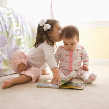 Caucasian girl children sitting on bedroom floor looking at book.