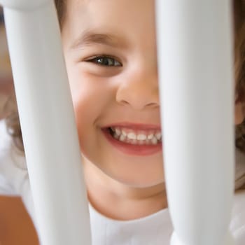Caucasian girl toddler smiling and peering between railing.